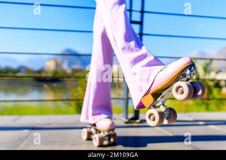 photo de près des pieds d'une femme dans un pantalon rose évasé patinant sur des rouleaux dans le parc Banque D'Images