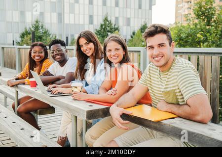Groupe multiracial d'adolescents heureux regardant la caméra, souriant détendu ensemble à l'extérieur du campus de l'université prenant une pause. Réunion de jeunes et de gens d'université amusant appréciant la lumière du soleil étudiant et posant dans l'attitude positive à l'extérieur. Concept d'éducation. Photo de haute qualité Banque D'Images