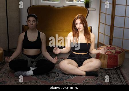 Une nouvelle mère sceptique convaincue de faire du yoga et de la méditation par un ami. Elle, une fille avec une expression agacée à côté d'une mère se détendant pendant qu'elle médit Banque D'Images