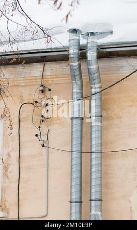 Deux tuyaux d'évacuation métalliques sur le fond du mur de la maison. Le toit du bâtiment dans la neige blanche. Nuageux, froid jour d'hiver, lumière douce. Banque D'Images