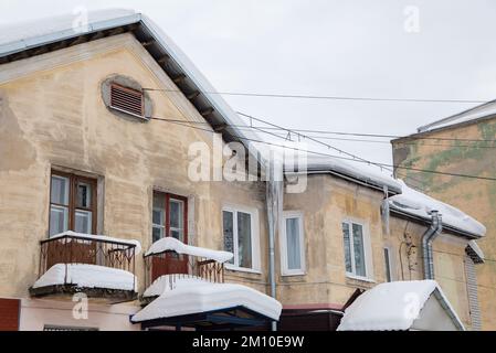 Toit recouvert de neige d'une vieille maison avec fenêtres, balcons et cheminées. Il y a de la neige et des glaçons sur le toit, sur fond de ciel gris. Nuageux, froid jour d'hiver, lumière douce. Banque D'Images