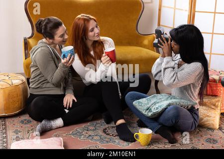 Jeunes amies qui s'amusent à l'intérieur en prenant des photos les unes des autres avec un appareil photo polarisé vintage. Groupe multiethnique de la génération du millénaire Banque D'Images