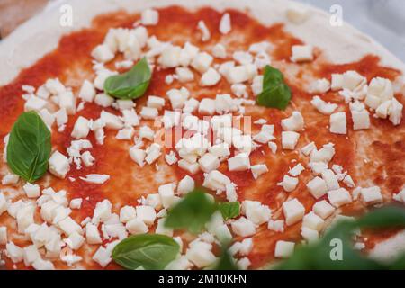 Préparation de la pizza avec sauce tomate, mozzarella fraîche et feuilles de basilic vert sur une planche de bois, gros plan Banque D'Images