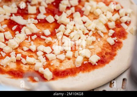 Préparer une pizza avec une sauce tomate et de la mozzarella fraîche sur une planche de bois avec des ingrédients et des outils autour, gros plan Banque D'Images