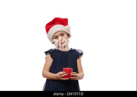 Jolie fille portant le chapeau du Père Noël et élégante robe bleue, tenant une bougie rouge allumée et souriant un beau sourire Banque D'Images