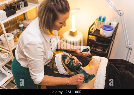 Belle femme blonde caucasienne appréciant obtenir un traitement professionnel du visage avec masque d'algues vertes à la boutique de beauté. . Photo de haute qualité Banque D'Images