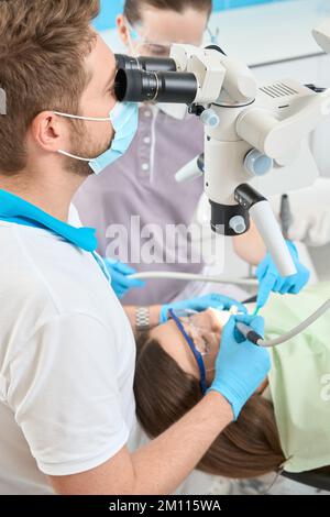 Dentiste qualifié effectuant une intervention dentaire sur une patiente Banque D'Images