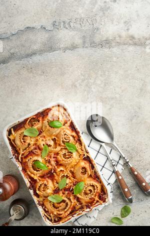 Lasagnes. Pâtes de lasagne faites maison rotolo cuire avec sauce tomate, fromage à la crème et basilic sur une poêle blanche sur fond d'ardoise légère, de pierre ou de béton. JE Banque D'Images