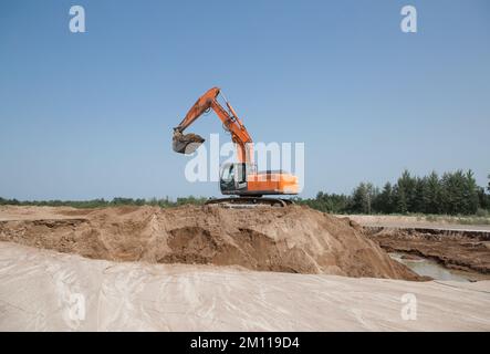 Grande pelle hydraulique de construction à chenilles orange sur un chantier de construction dans une fosse de sable tout en travaillant sur une journée ensoleillée contre un ciel bleu. image industrielle Banque D'Images