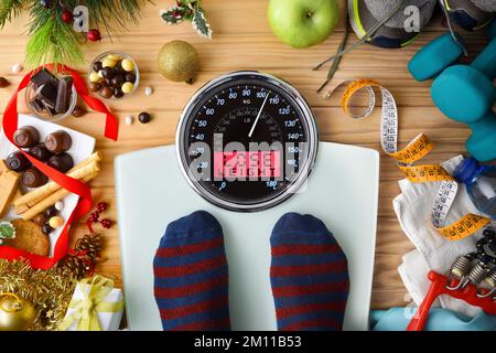 Personne pesant sur une balance après les vacances de Noël avec message perdre du poids sur fond de bois avec des bonbons et des équipements sportifs. Vue de dessus. Banque D'Images