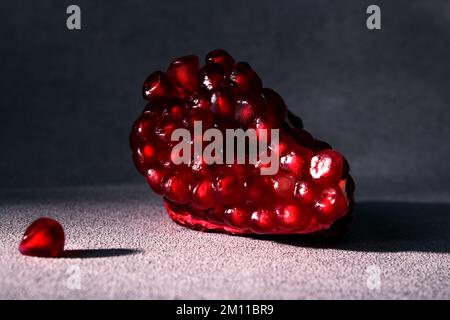 Une tranche de grenade mûre rouge sur fond gris. Fruits d'hiver de saison. Source de fer Banque D'Images