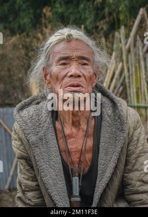Ziro, Arunachal Pradesh, Inde - 02 19 2013 : Portrait de l'ancien homme tribal des Apatani avec tatouage traditionnel au menton et cheveu frontal assis à l'extérieur Banque D'Images
