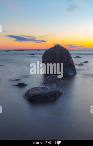 Heure bleue après le coucher du soleil sur la mer Baltique rocheuse coût. Petites pierres et gros rochers dans la mer. Photo à exposition longue. Banque D'Images