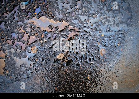 Taches d'huile dues à des fuites dans le moteur de la voiture. L'huile après la pluie fait des taches avec des reflets arc-en-ciel spectre de réfraction du soleil. Banque D'Images