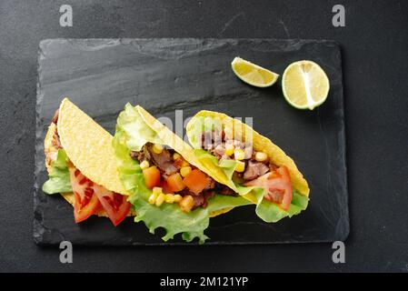 Tacos mexicains avec bœuf, légumes et salsa. Tacos al curé sur une planche de bois sur fond noir. Vue de dessus avec espace de copie. Banque D'Images