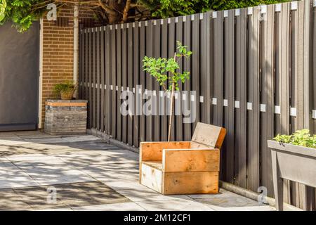 un petit arbre poussant dans une boîte sur le trottoir à côté d'une clôture en bois qui a été peint avec de la peinture blanche Banque D'Images