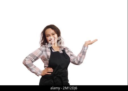 Femme afro-américaine serveuse dans le tablier du chef noir, souriant à l'appareil photo, tenant un espace de copie pour votre texte publicitaire Banque D'Images