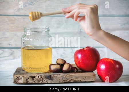 pot de miel d'abeille avec un balancier de miel sur un panneau en bois antique, atmosphère d'automne avec châtaignes et quelques pommes rouges Banque D'Images