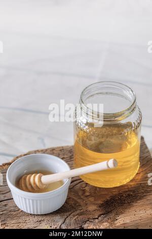 pot en verre de miel d'abeille avec une petite tasse et un balancier de miel sur un panneau en bois antique Banque D'Images