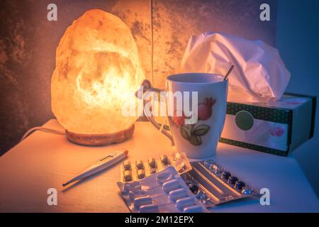 table de chevet éclairée par une lampe à sel, avec des médicaments et un thermomètre pour la fièvre Banque D'Images