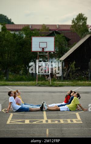 Ivano-Frankivsk, Ukraine 14 juillet 2022: Portrait d'un groupe d'adolescents sur un terrain sportif, enfants assis sur un terrain de basket avec leurs pieds res Banque D'Images