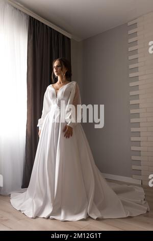 Ivano-Frankivsk, Ukraine 26 juin 2021: Robe blanche de mariage pour la mariée le jour du mariage, la mariée tente sur la robe près de la fenêtre. Banque D'Images