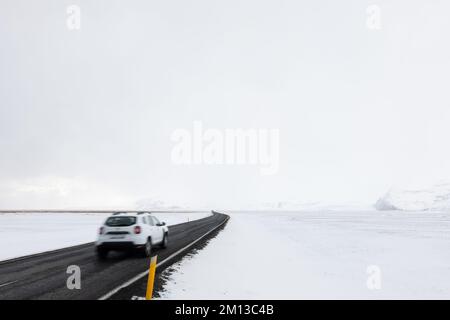 Voiture conduite sur route menant à travers le paysage enneigé gelé du sud de l'Islande en hiver Banque D'Images
