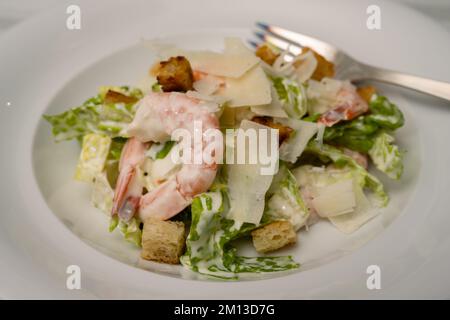 Salade César aux crevettes, copeaux de parmesan, croûtons et vinaigrette à l'ail sur une assiette blanche Banque D'Images