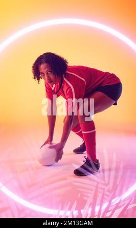 Mélange de joueuses de rugby biraciales avec balle courbant sur un cercle lumineux et des plantes Banque D'Images