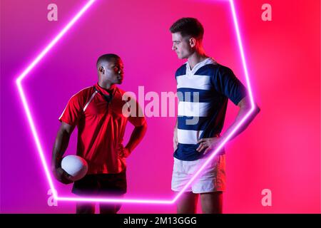 Les joueurs de rugby multiraciaux masculins se regardent les uns les autres par un hexagone lumineux sur fond rose Banque D'Images