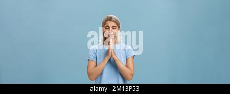 Une fille européenne à la fois belle et fidèle avec des cheveux blonds souriants mignon et tendre tenant les mains dans la prière tout en faisant le souhait j'espère croire dieu Banque D'Images