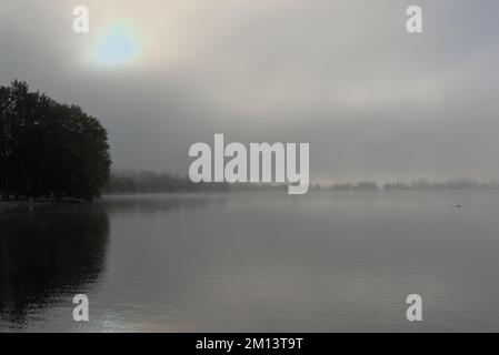 Un matin d'automne très brumeux avec un soleil pâle se levant sur un lac brumeux de Dow. Ottawa, ON, Canada. Banque D'Images