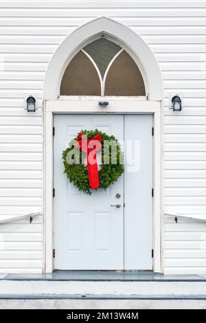 Belle couronne de Noël faite maison construite de bourgs d'épicéa frais accrochés à la porte d'une église de campagne de 19th siècles en Nouvelle-Écosse. Banque D'Images