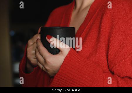 gros plan des mains des femmes tenant une tasse de café grise, portant un pull doux et chaud rouge Banque D'Images