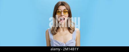 Prise de vue à la taille d'une femme caucasienne excitée, surprise et émotive et charismatique dans les lunettes de soleil tendance ouvrant la bouche de l'étonnement et la joie regarder à l'appareil photo Banque D'Images