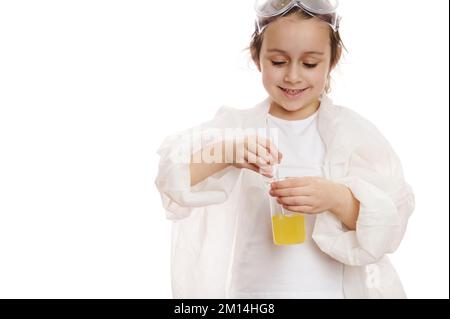 Détails : mains d'enfant mélangeant un produit chimique liquide jaune dans un bécher, avec un bâton de laboratoire en classe de chimie, sur fond blanc Banque D'Images