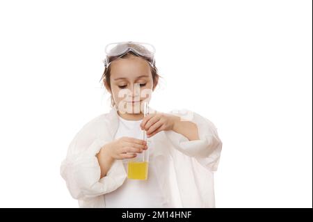 Petite fille, jeune chimiste en blouse de laboratoire, utilisant un bâton de laboratoire, mélangeant un produit chimique liquide jaune avec des réactifs dans un bécher Banque D'Images