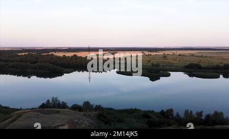 Vue aérienne sur la rivière qui se courbe le long des terres agricoles. Vue panoramique imprenable sur le paysage naturel avec des prairies luxuriantes et une rivière au coucher du soleil. Banque D'Images