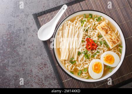 Soupe de miso ramen épicée avec tofu, champignons enoki, nouilles, oignon vert et piment gros plan dans un bol sur la table. Vue horizontale du dessus Banque D'Images