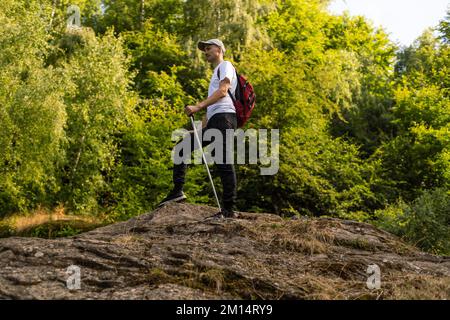 Jeune randonneur avec sac à dos et bâtons de randonnée debout sur le bord de la falaise et regardant les montagnes en été en plein air. Banque D'Images