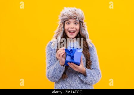 surprise enfant avec l'achat dans le chapeau. lendemain de noël. jeune fille en tricot sur fond jaune. Banque D'Images