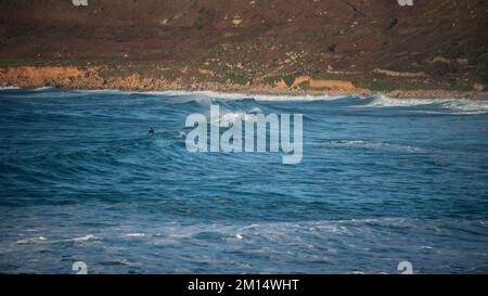 Des surfeurs non identifiés qui surfent sur les vagues à Sennen Cove, dans les Cornouailles, à la fin du coucher du soleil Banque D'Images