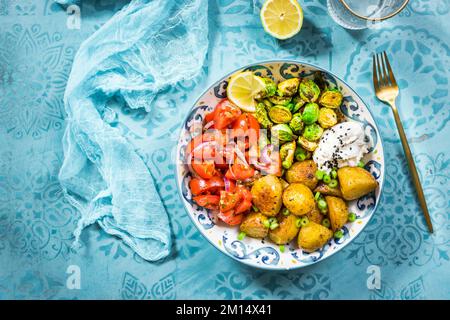 Bol Bouddha, nourriture saine et équilibrée avec pommes de terre au four, pousses de Bruxelles et salade de tomates Banque D'Images