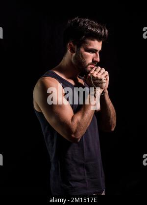 Homme spirituel priant avec rosaire dans l'obscurité Banque D'Images