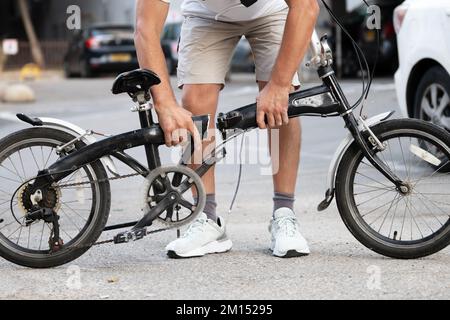Homme tenant un vélo avec un cadre cassé en moitié dans la rue Banque D'Images
