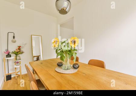 une salle à manger avec des tournesols dans un vase en verre sur la table en bois et deux chaises au mur est blanche Banque D'Images