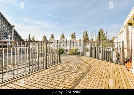 une terrasse en bois avec des rambardes en métal et des bâtiments en arrière-plan par temps ensoleillé, prise d'un balcon d'appartement Banque D'Images