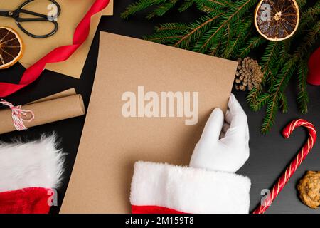 Le Père Noël lisant les lettres des enfants sur le bureau. Vue de dessus des mains de Jolly Father tenant une page de papier marron vierge. Vue depuis le dessus de la table en bois avec Banque D'Images