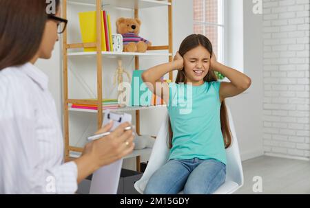 Une jeune fille frustrée et confuse ferme ses oreilles assise sur une chaise devant le psychologue de l'école. Banque D'Images