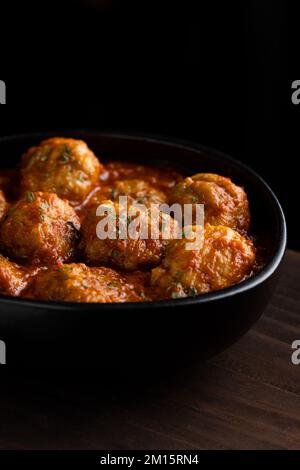 De dessus de bol noir avec de délicieux boulettes de viande dans la sauce tomate avec des herbes placées sur le bois dans la pièce sombre Banque D'Images